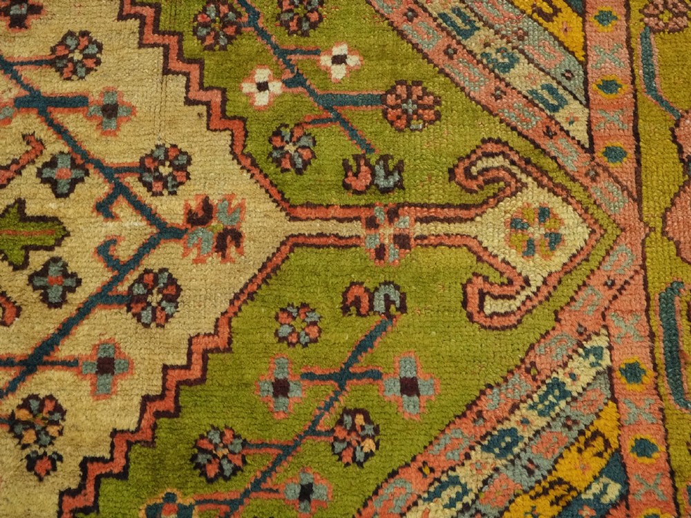 An antique Turkish Oushak wool carpet featuring an olive green field with a central cream and coral diamond medallion surrounded by detailed geometric borders. View XII