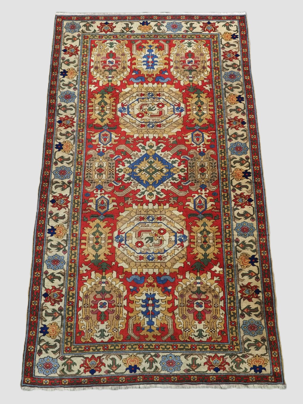 An antique hand-knotted wool rug with a central red field featuring geometric Karabagh blossom motifs and multi-tiered decorative borders.