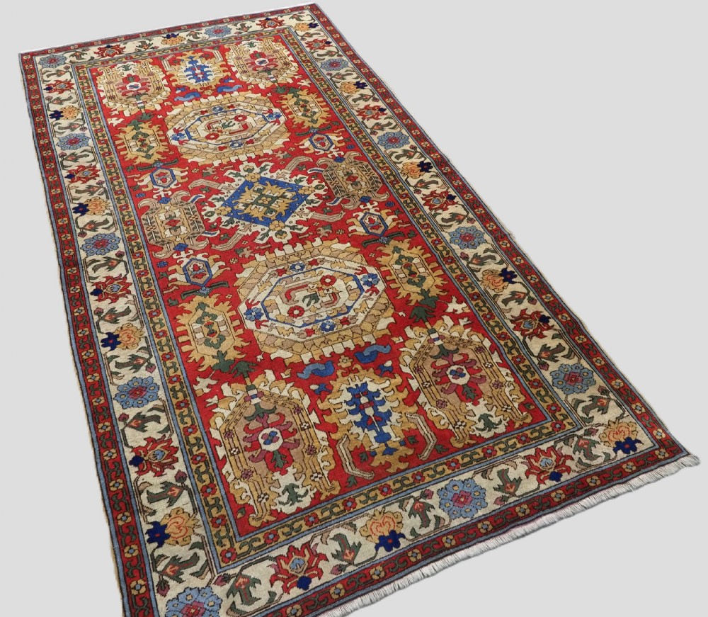 An antique hand-knotted wool rug with a central red field featuring geometric Karabagh blossom motifs and multi-tiered decorative borders. View II