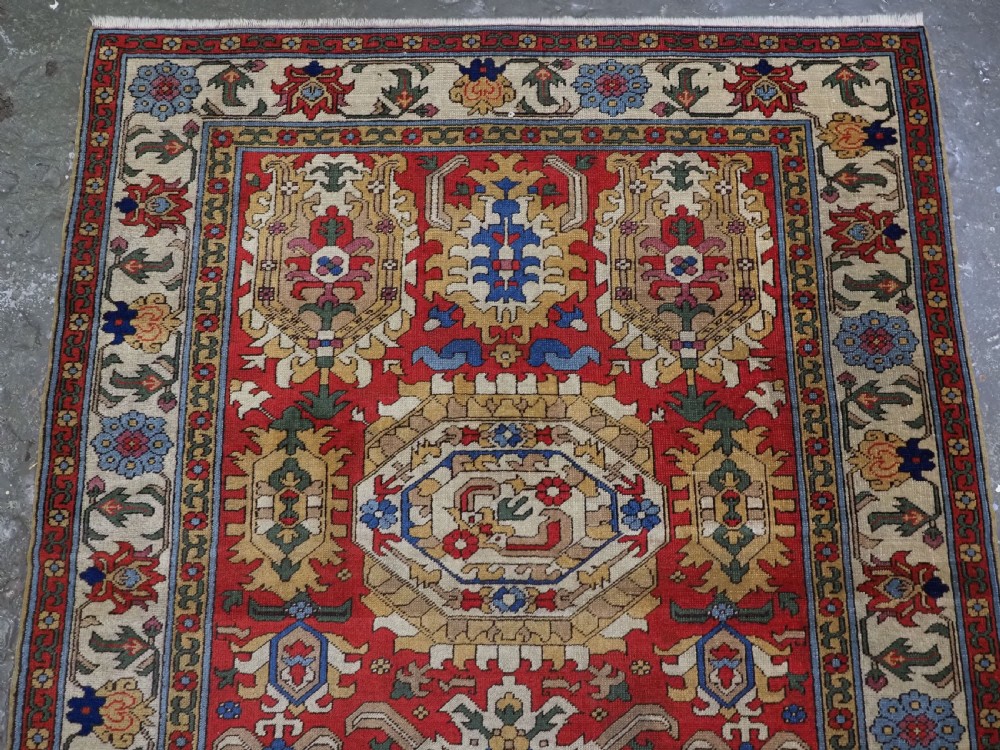 An antique hand-knotted wool rug with a central red field featuring geometric Karabagh blossom motifs and multi-tiered decorative borders. View III