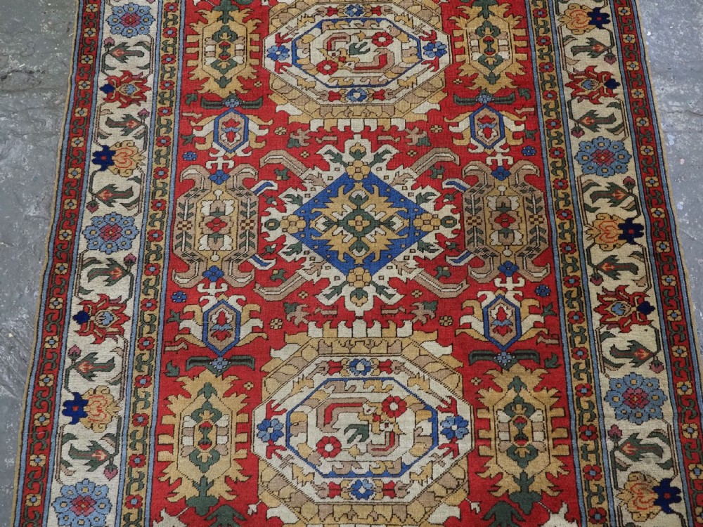 An antique hand-knotted wool rug with a central red field featuring geometric Karabagh blossom motifs and multi-tiered decorative borders. View IV