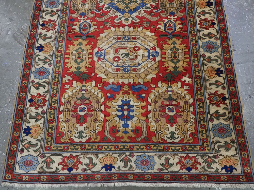 An antique hand-knotted wool rug with a central red field featuring geometric Karabagh blossom motifs and multi-tiered decorative borders. View V