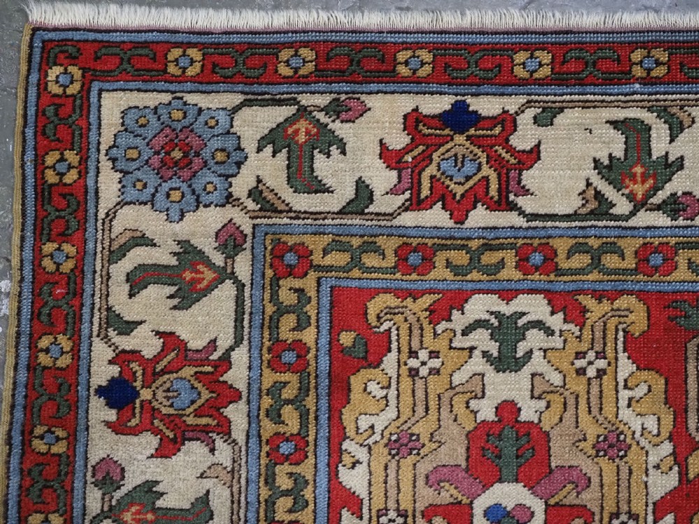 An antique hand-knotted wool rug with a central red field featuring geometric Karabagh blossom motifs and multi-tiered decorative borders. View VI