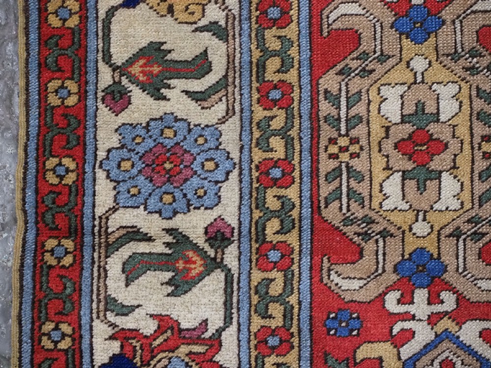 An antique hand-knotted wool rug with a central red field featuring geometric Karabagh blossom motifs and multi-tiered decorative borders. View VII