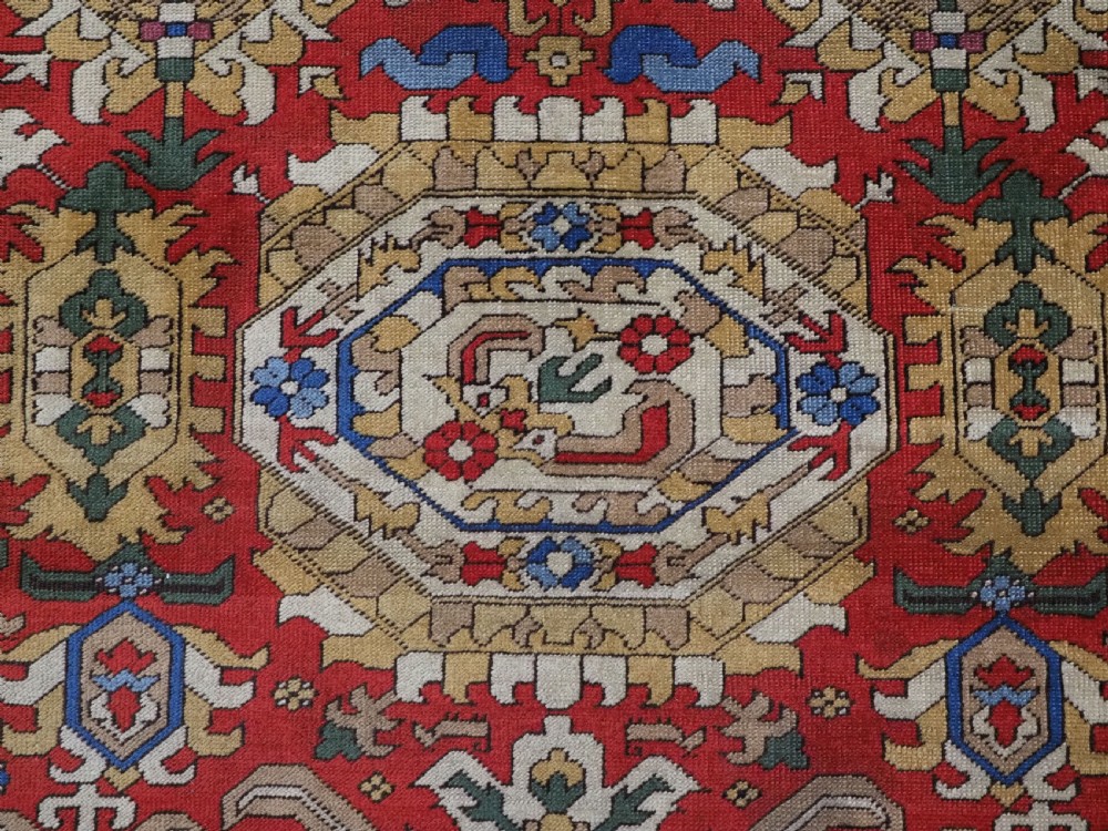 An antique hand-knotted wool rug with a central red field featuring geometric Karabagh blossom motifs and multi-tiered decorative borders. View IX