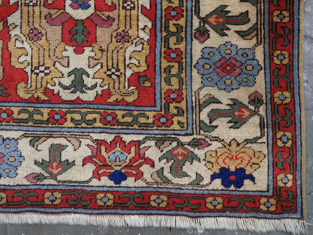 An antique hand-knotted wool rug with a central red field featuring geometric Karabagh blossom motifs and multi-tiered decorative borders. View XV
