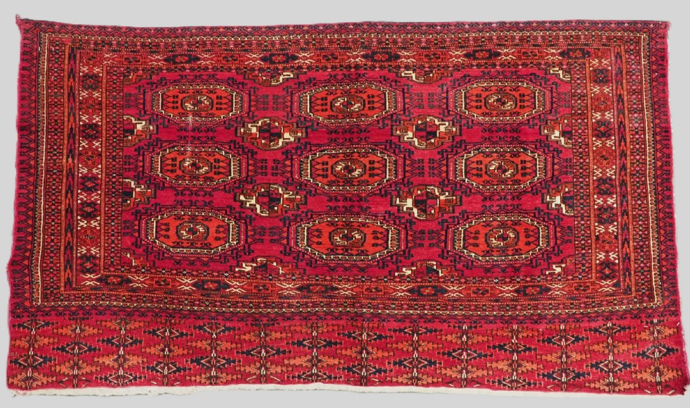 A rectangular deep red hand-knotted wool Tekke Turkmen chuval face featuring nine octagonal turreted guls surrounded by geometric borders.