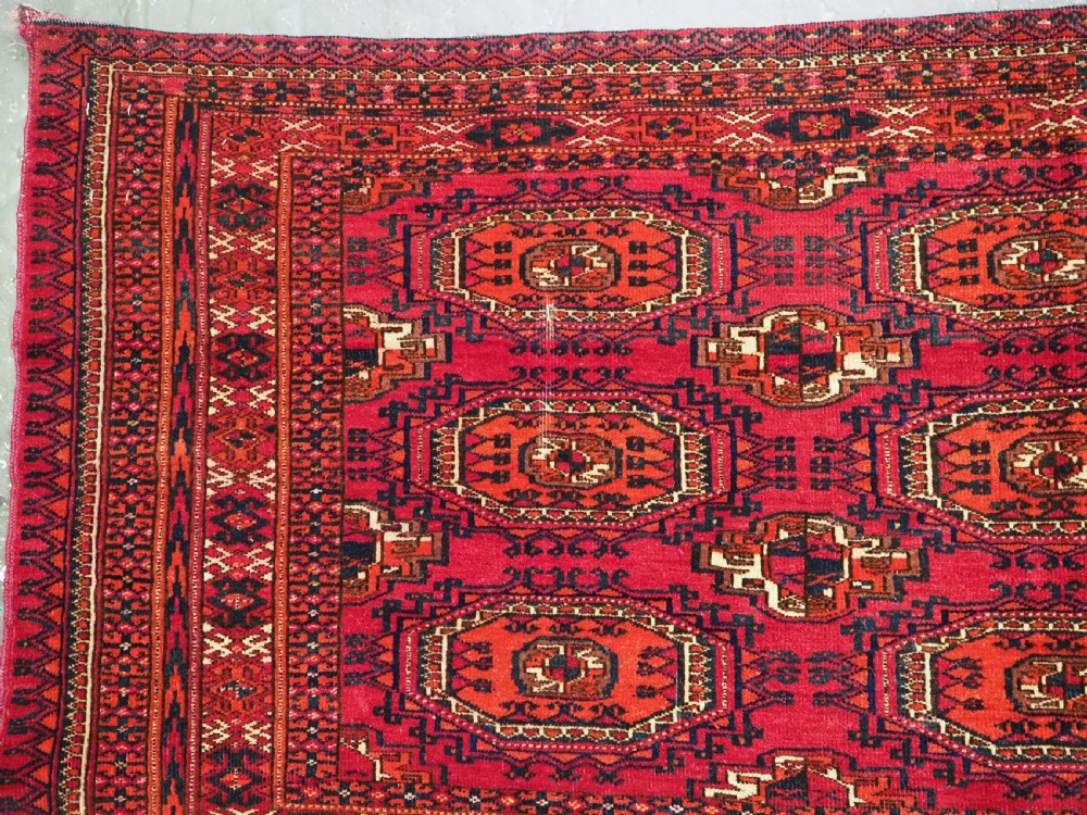 A rectangular deep red hand-knotted wool Tekke Turkmen chuval face featuring nine octagonal turreted guls surrounded by geometric borders. View III