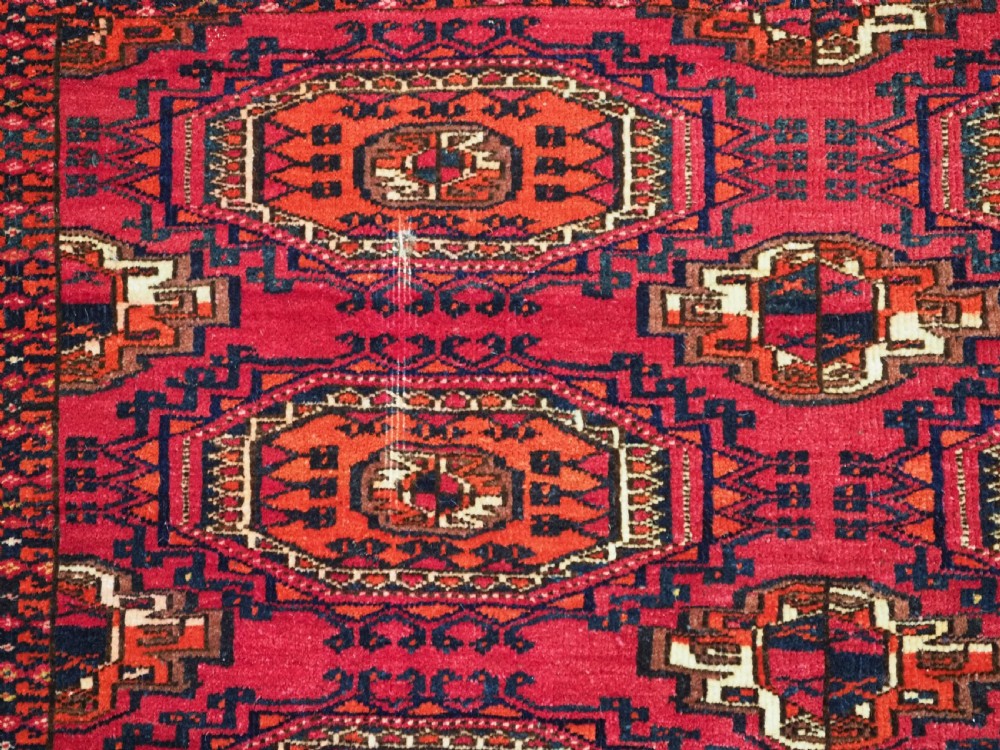 A rectangular deep red hand-knotted wool Tekke Turkmen chuval face featuring nine octagonal turreted guls surrounded by geometric borders. View V