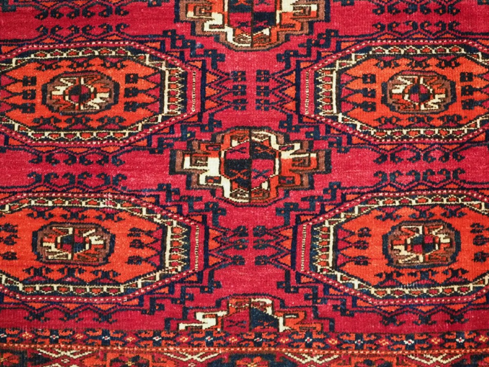 A rectangular deep red hand-knotted wool Tekke Turkmen chuval face featuring nine octagonal turreted guls surrounded by geometric borders. View VI