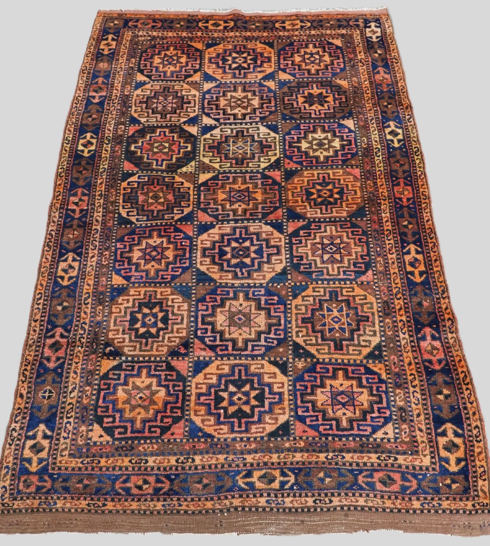 An antique Kurdish Kordi hand-knotted wool rug decorated with repeating octagonal Memlinc guls in navy blue, terracotta, and ochre.