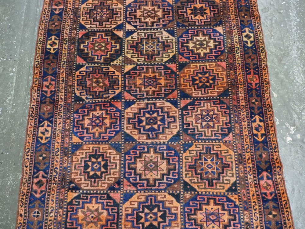An antique Kurdish Kordi hand-knotted wool rug decorated with repeating octagonal Memlinc guls in navy blue, terracotta, and ochre. View IV
