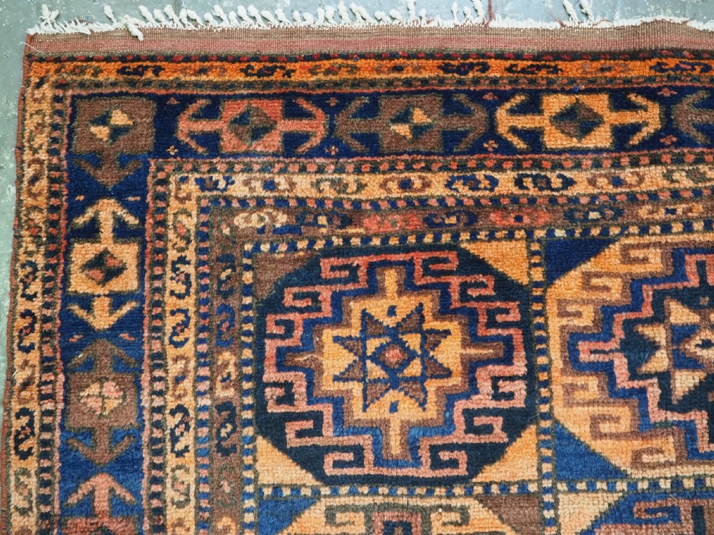 An antique Kurdish Kordi hand-knotted wool rug decorated with repeating octagonal Memlinc guls in navy blue, terracotta, and ochre. View VI