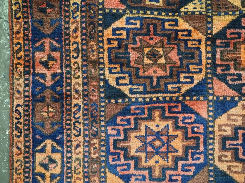 An antique Kurdish Kordi hand-knotted wool rug decorated with repeating octagonal Memlinc guls in navy blue, terracotta, and ochre. View VII