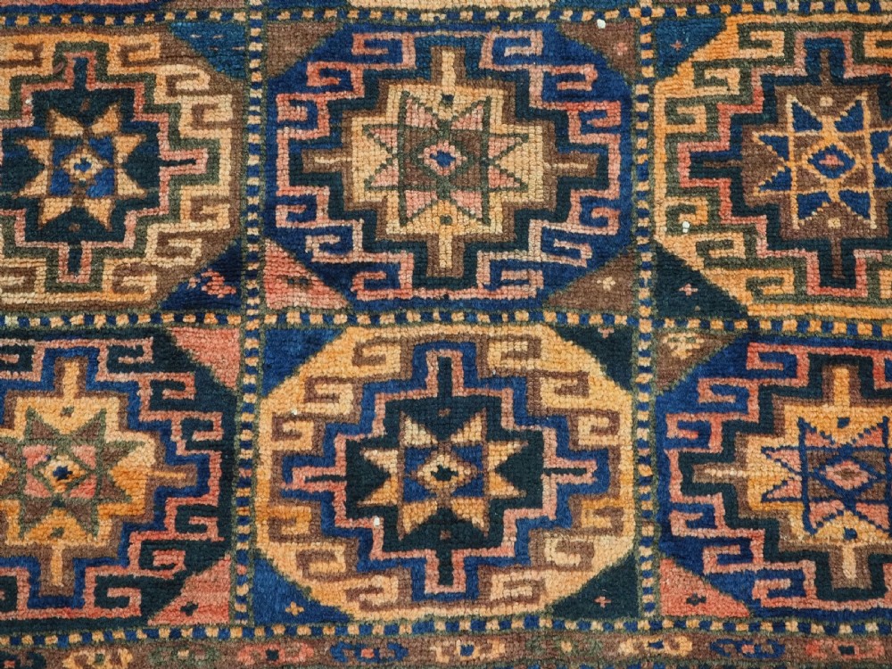 An antique Kurdish Kordi hand-knotted wool rug decorated with repeating octagonal Memlinc guls in navy blue, terracotta, and ochre. View X