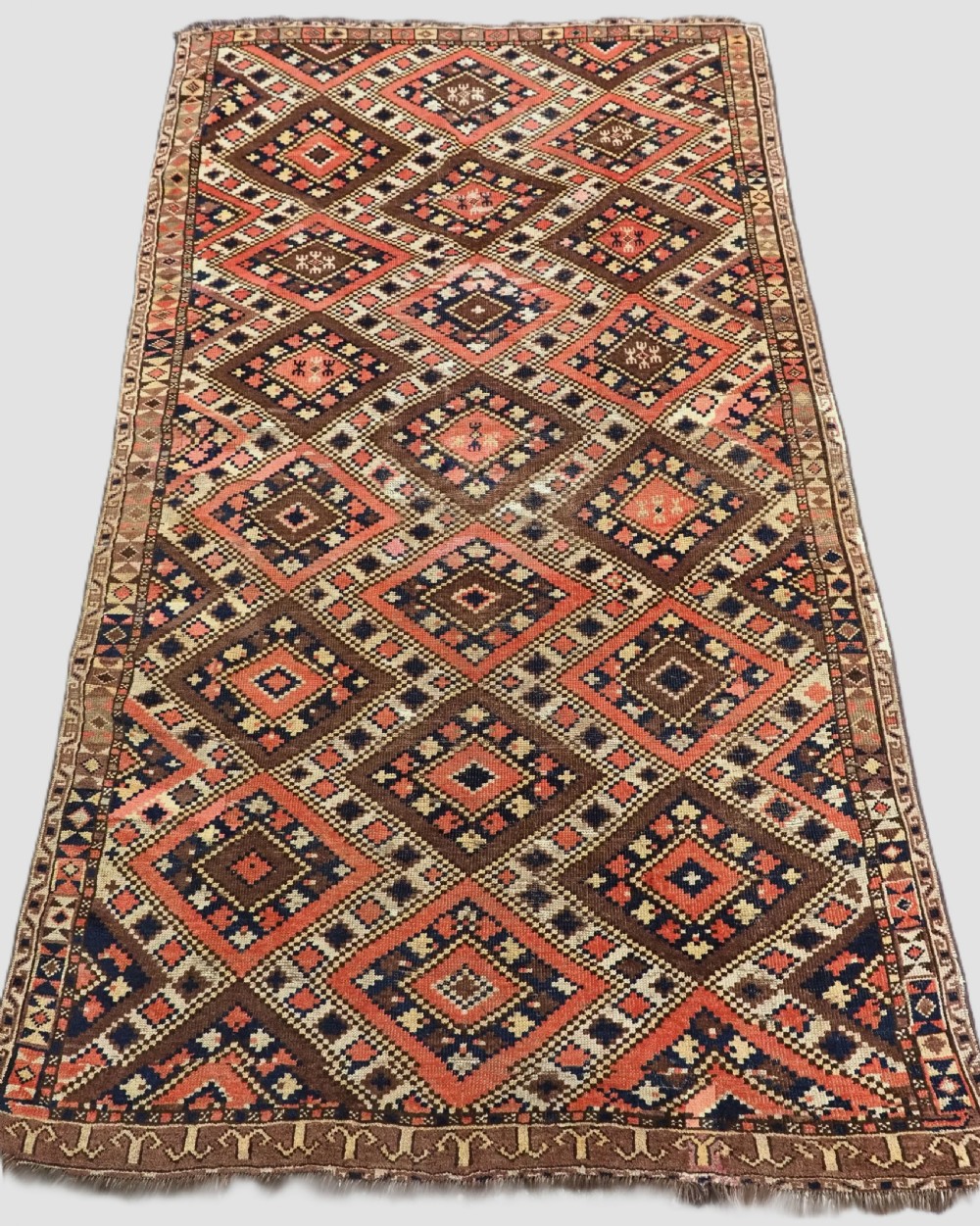An antique Central Asian hand-woven wool rug featuring a repeating diamond lattice pattern in terracotta, dark brown, cream, and deep blue.