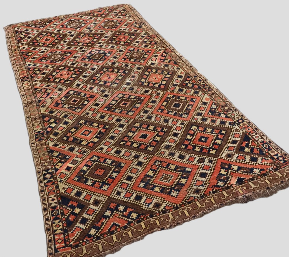 An antique Central Asian hand-woven wool rug featuring a repeating diamond lattice pattern in terracotta, dark brown, cream, and deep blue. View II