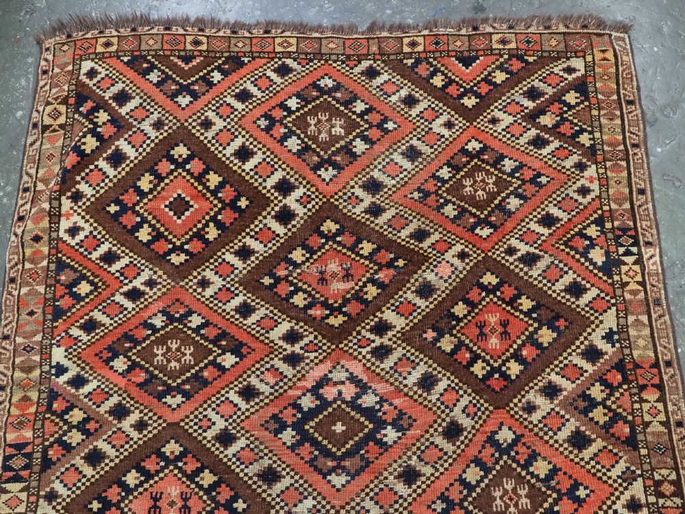An antique Central Asian hand-woven wool rug featuring a repeating diamond lattice pattern in terracotta, dark brown, cream, and deep blue. View III