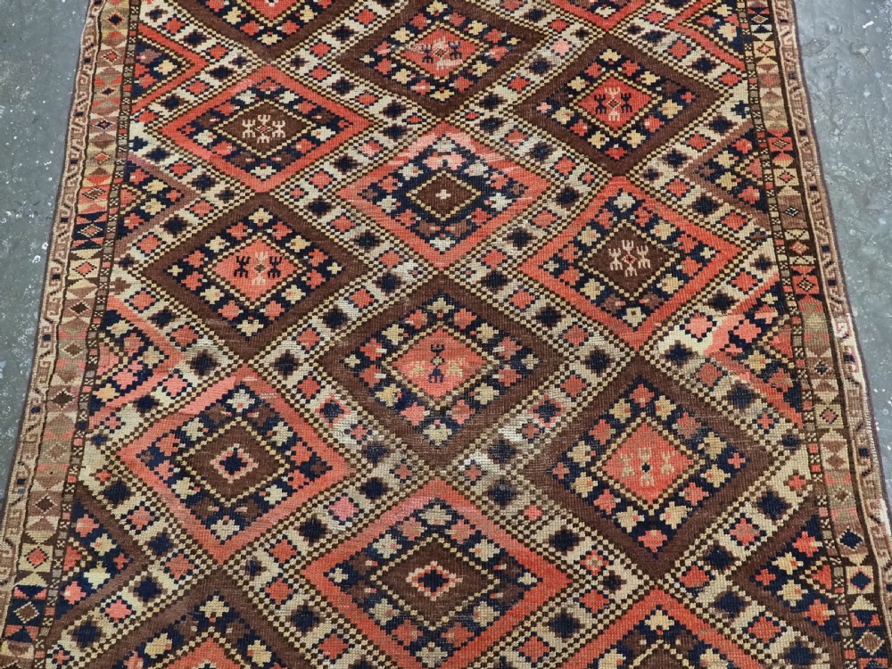 An antique Central Asian hand-woven wool rug featuring a repeating diamond lattice pattern in terracotta, dark brown, cream, and deep blue. View IV
