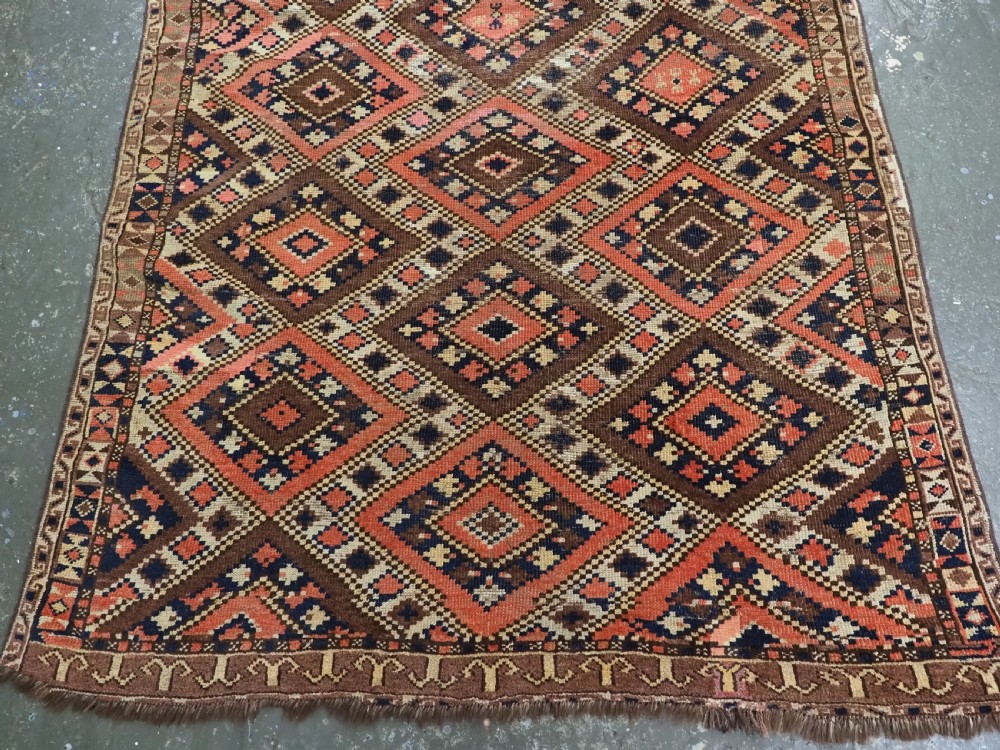 An antique Central Asian hand-woven wool rug featuring a repeating diamond lattice pattern in terracotta, dark brown, cream, and deep blue. View V