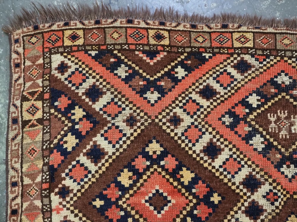 An antique Central Asian hand-woven wool rug featuring a repeating diamond lattice pattern in terracotta, dark brown, cream, and deep blue. View VI