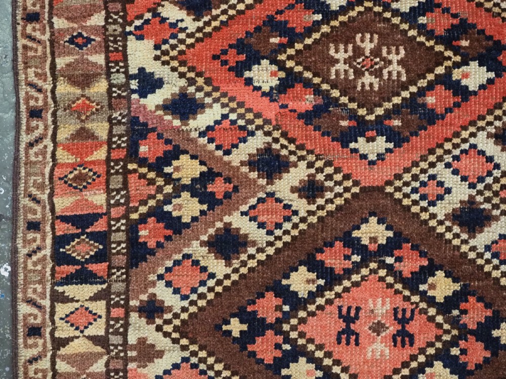 An antique Central Asian hand-woven wool rug featuring a repeating diamond lattice pattern in terracotta, dark brown, cream, and deep blue. View VII