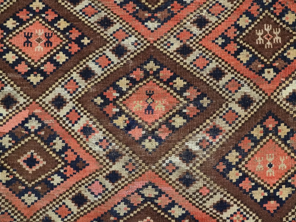 An antique Central Asian hand-woven wool rug featuring a repeating diamond lattice pattern in terracotta, dark brown, cream, and deep blue. View IX