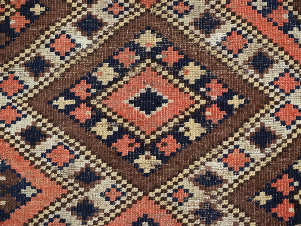 An antique Central Asian hand-woven wool rug featuring a repeating diamond lattice pattern in terracotta, dark brown, cream, and deep blue. View X