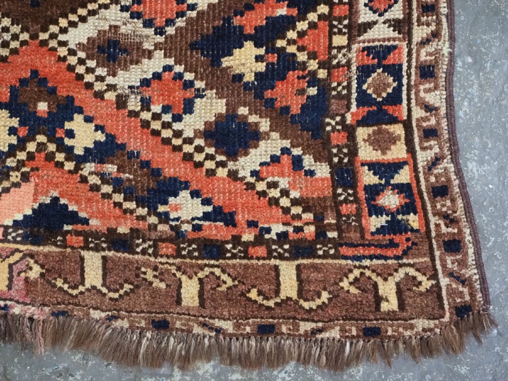An antique Central Asian hand-woven wool rug featuring a repeating diamond lattice pattern in terracotta, dark brown, cream, and deep blue. View XI