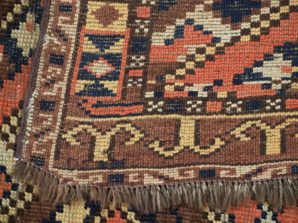 An antique Central Asian hand-woven wool rug featuring a repeating diamond lattice pattern in terracotta, dark brown, cream, and deep blue. View XII
