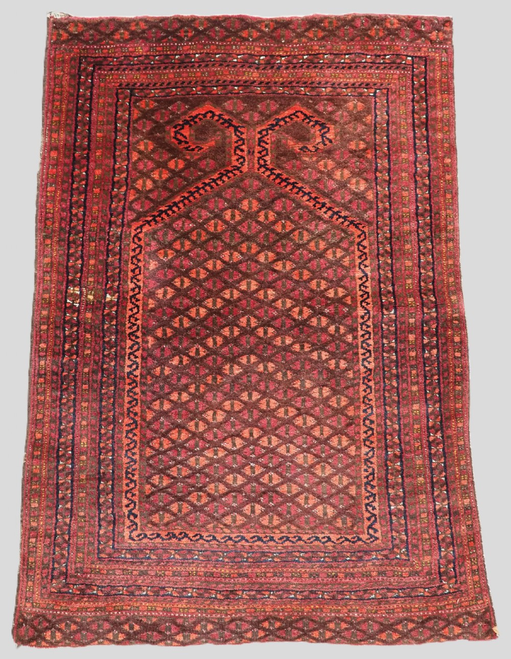 An antique red wool Turkmen prayer rug featuring a geometric diamond lattice pattern and a distinctive rams horn arch at the top.