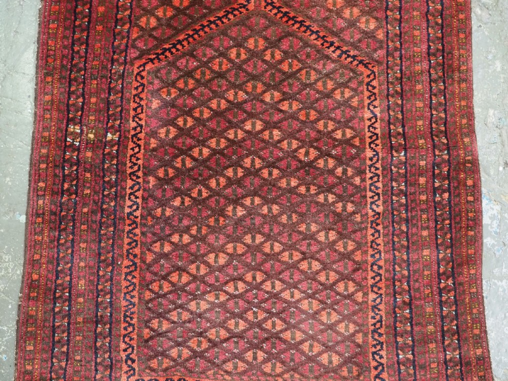 An antique red wool Turkmen prayer rug featuring a geometric diamond lattice pattern and a distinctive rams horn arch at the top. View IV