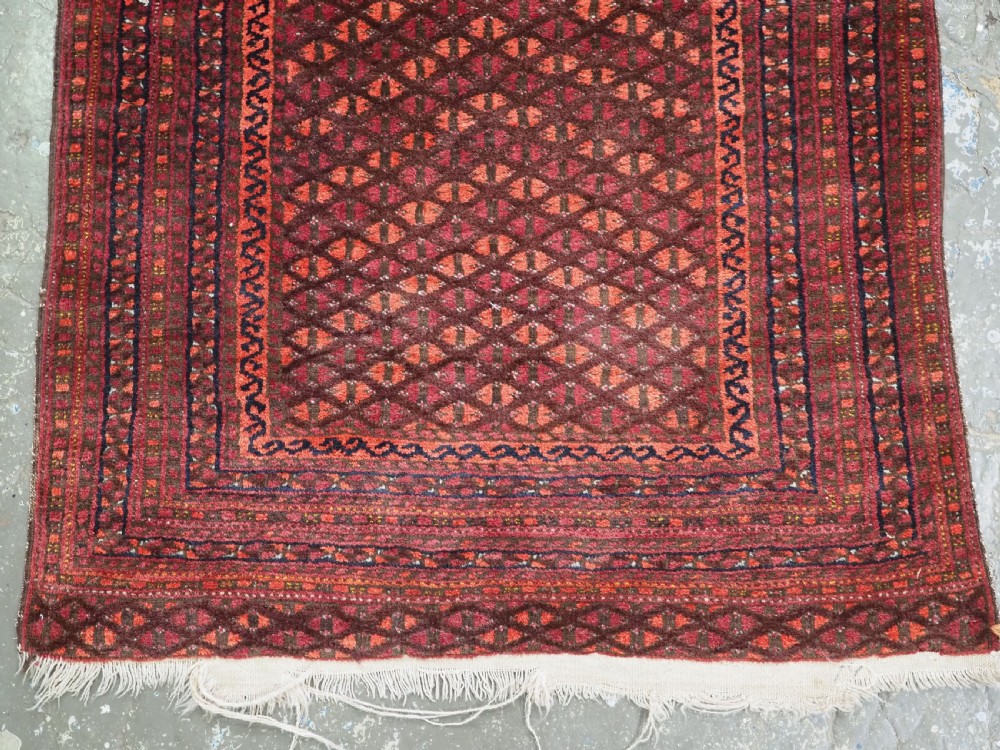 An antique red wool Turkmen prayer rug featuring a geometric diamond lattice pattern and a distinctive rams horn arch at the top. View V