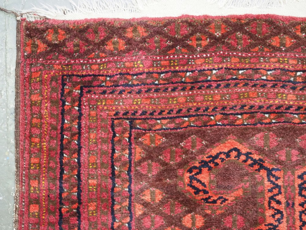An antique red wool Turkmen prayer rug featuring a geometric diamond lattice pattern and a distinctive rams horn arch at the top. View VI
