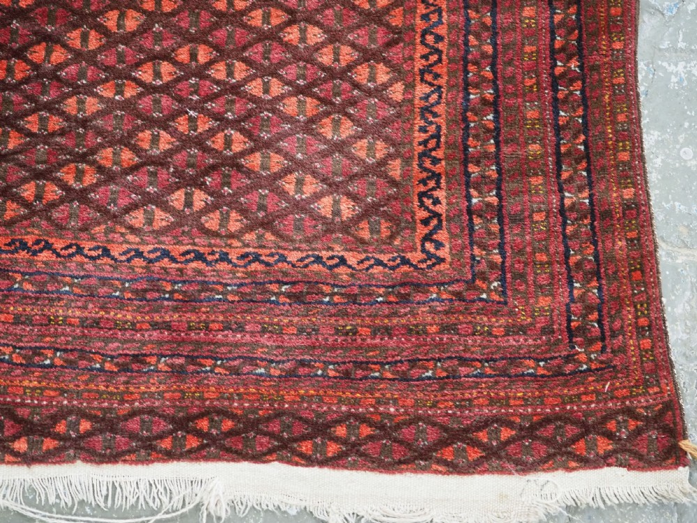 An antique red wool Turkmen prayer rug featuring a geometric diamond lattice pattern and a distinctive rams horn arch at the top. View IX