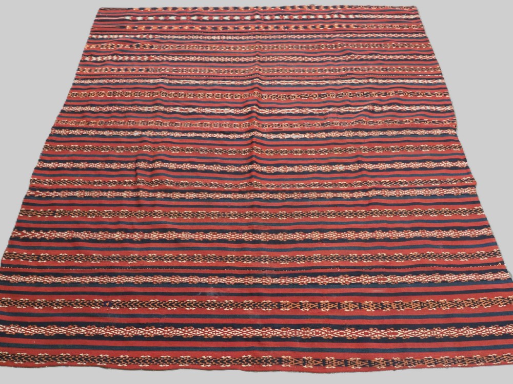 An antique Uzbek Gajeri flatweave kilim rug featuring horizontal bands of terracotta red, navy blue, and cream geometric motifs.