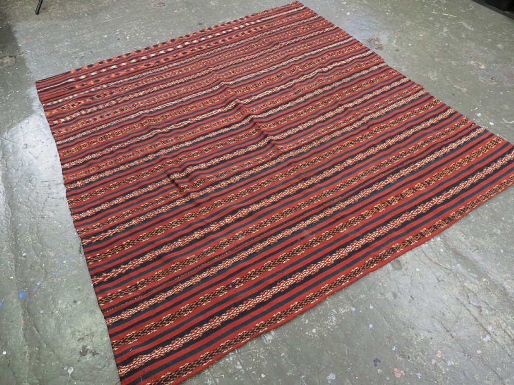 An antique Uzbek Gajeri flatweave kilim rug featuring horizontal bands of terracotta red, navy blue, and cream geometric motifs. View II