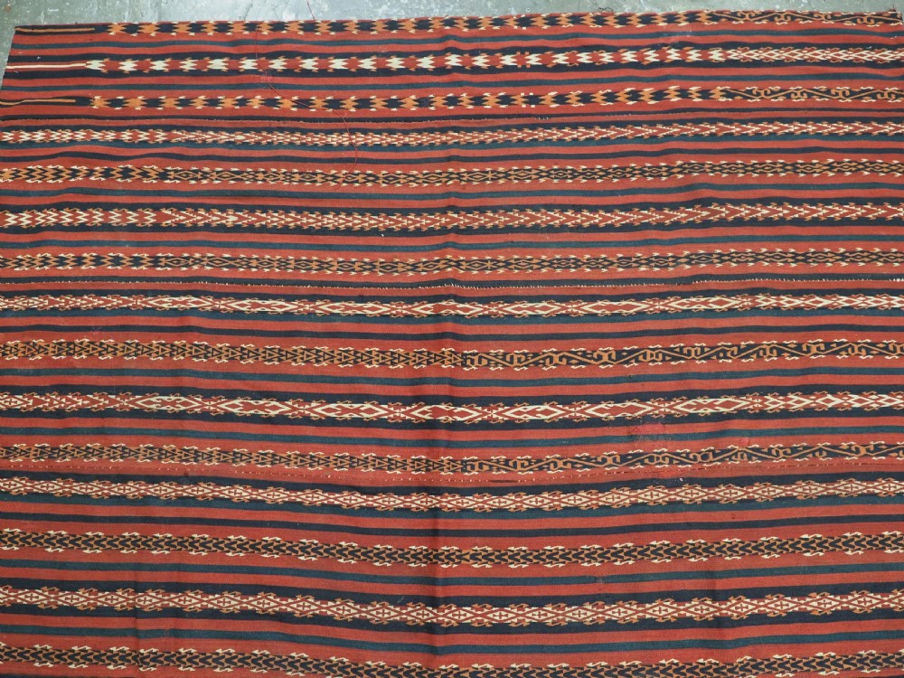 An antique Uzbek Gajeri flatweave kilim rug featuring horizontal bands of terracotta red, navy blue, and cream geometric motifs. View III
