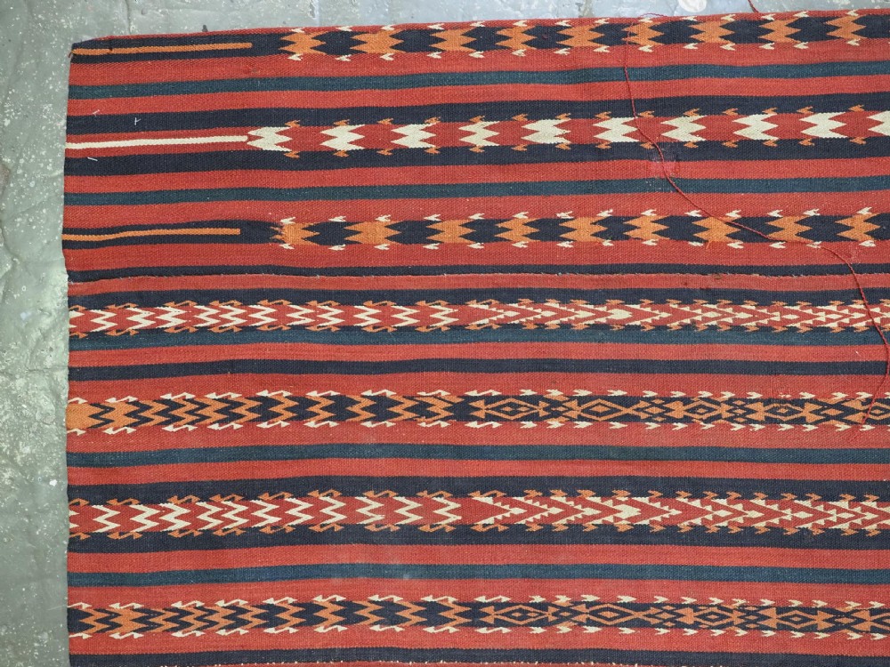 An antique Uzbek Gajeri flatweave kilim rug featuring horizontal bands of terracotta red, navy blue, and cream geometric motifs. View IV