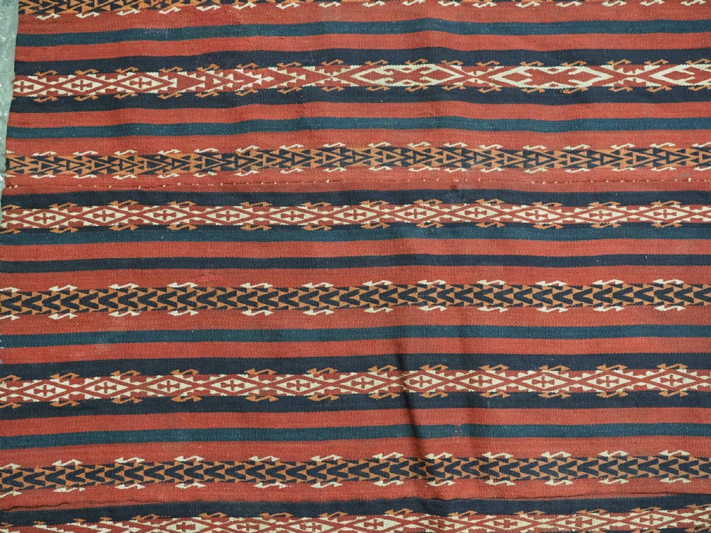 An antique Uzbek Gajeri flatweave kilim rug featuring horizontal bands of terracotta red, navy blue, and cream geometric motifs. View V