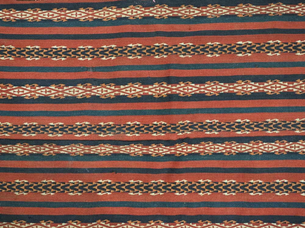 An antique Uzbek Gajeri flatweave kilim rug featuring horizontal bands of terracotta red, navy blue, and cream geometric motifs. View VI