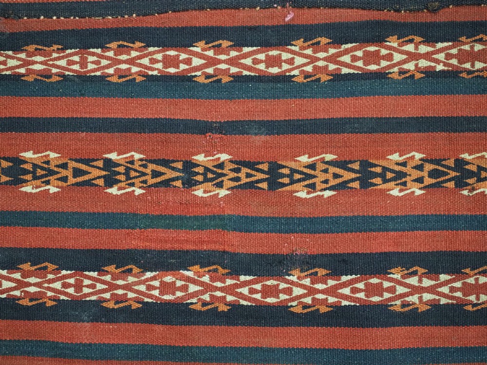 An antique Uzbek Gajeri flatweave kilim rug featuring horizontal bands of terracotta red, navy blue, and cream geometric motifs. View VII