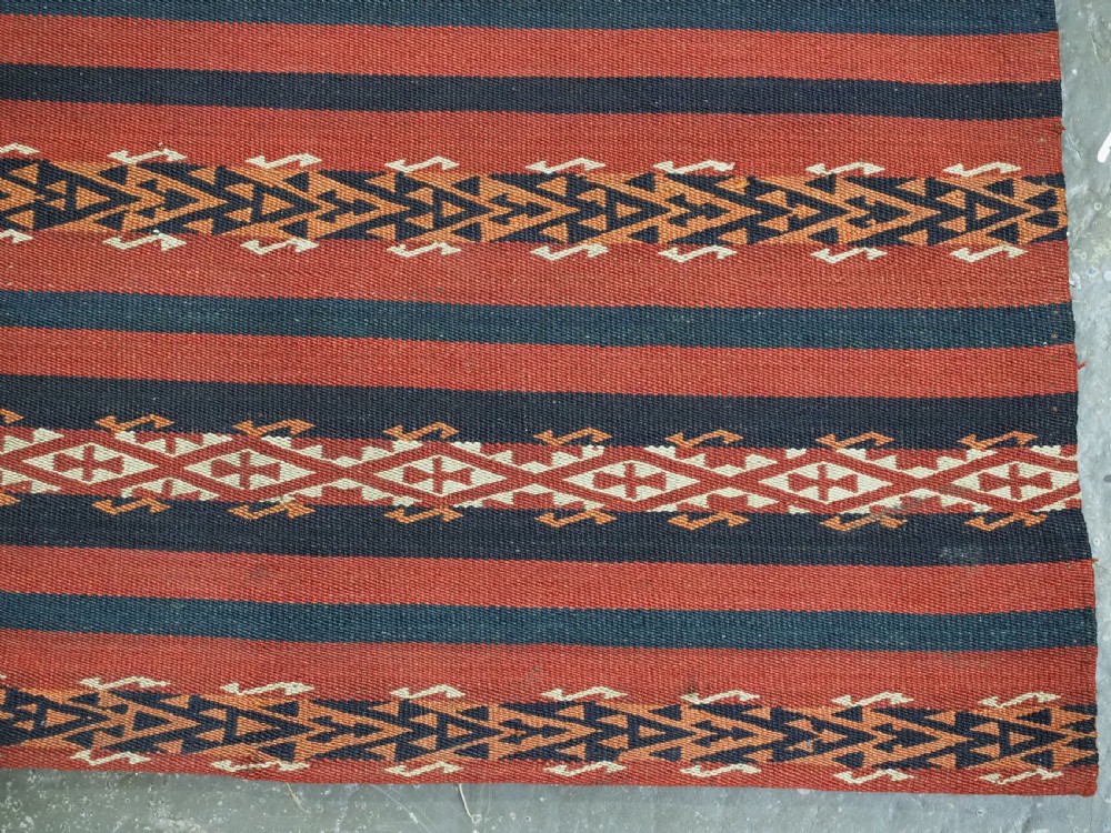An antique Uzbek Gajeri flatweave kilim rug featuring horizontal bands of terracotta red, navy blue, and cream geometric motifs. View VIII