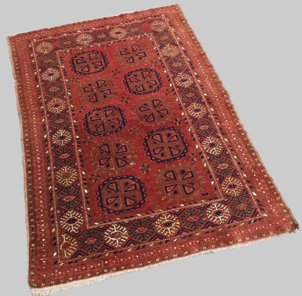 A rectangular hand-knotted wool rug featuring repeating octagonal gul motifs in dark blue and brown set against a deep red field with geometric patterned borders. View II