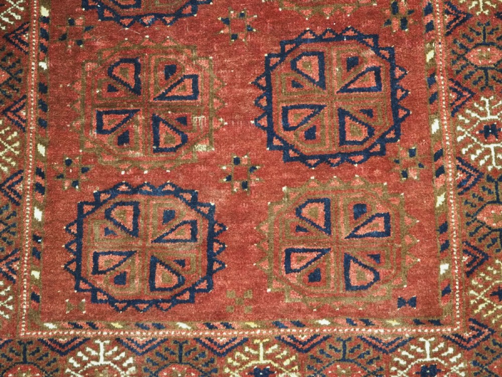 A rectangular hand-knotted wool rug featuring repeating octagonal gul motifs in dark blue and brown set against a deep red field with geometric patterned borders. View VIII