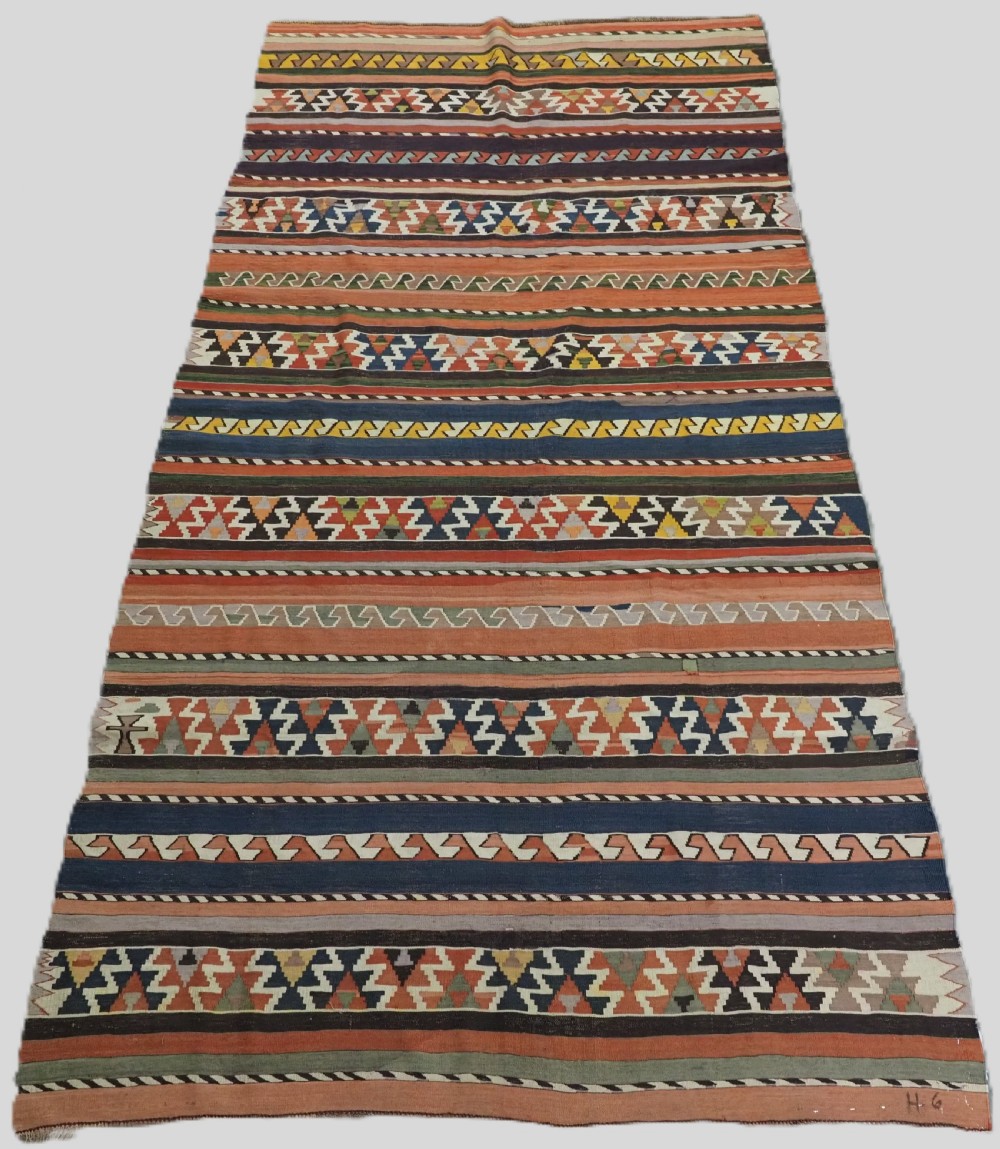 An antique handwoven wool Caucasian Shirvan kilim rug featuring horizontal bands filled with geometric serrated diamond and zig-zag patterns in terracotta, blue, green, and yellow tones.