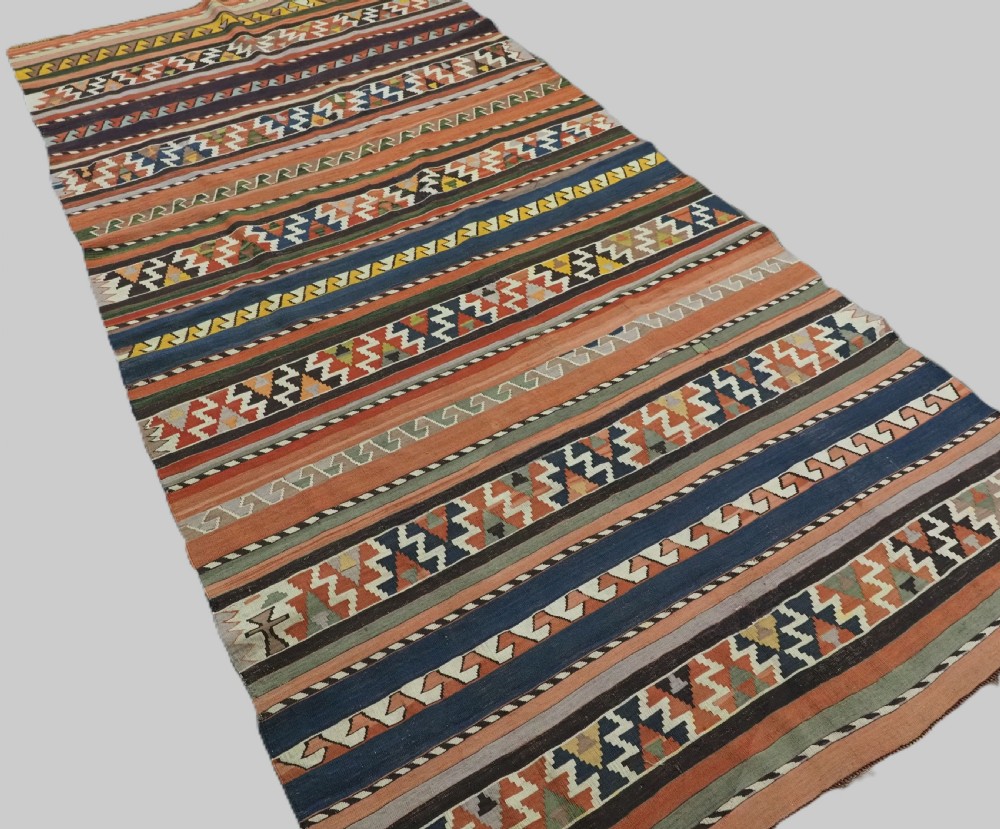 An antique handwoven wool Caucasian Shirvan kilim rug featuring horizontal bands filled with geometric serrated diamond and zig-zag patterns in terracotta, blue, green, and yellow tones. View II