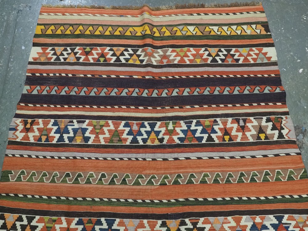 An antique handwoven wool Caucasian Shirvan kilim rug featuring horizontal bands filled with geometric serrated diamond and zig-zag patterns in terracotta, blue, green, and yellow tones. View III