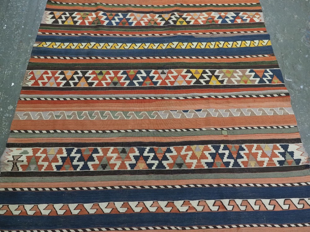 An antique handwoven wool Caucasian Shirvan kilim rug featuring horizontal bands filled with geometric serrated diamond and zig-zag patterns in terracotta, blue, green, and yellow tones. View V