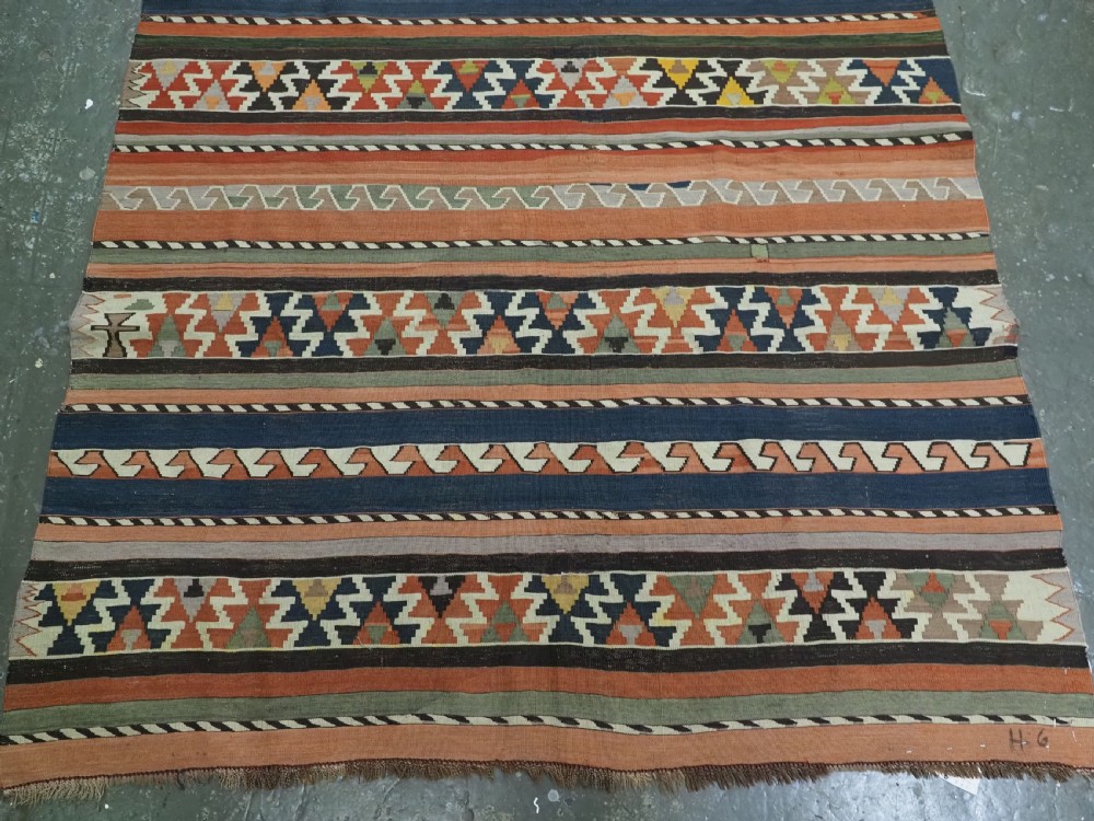 An antique handwoven wool Caucasian Shirvan kilim rug featuring horizontal bands filled with geometric serrated diamond and zig-zag patterns in terracotta, blue, green, and yellow tones. View VI